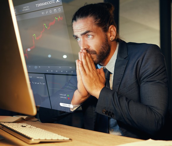 Worried-looking person viewing stock charts on a screen.