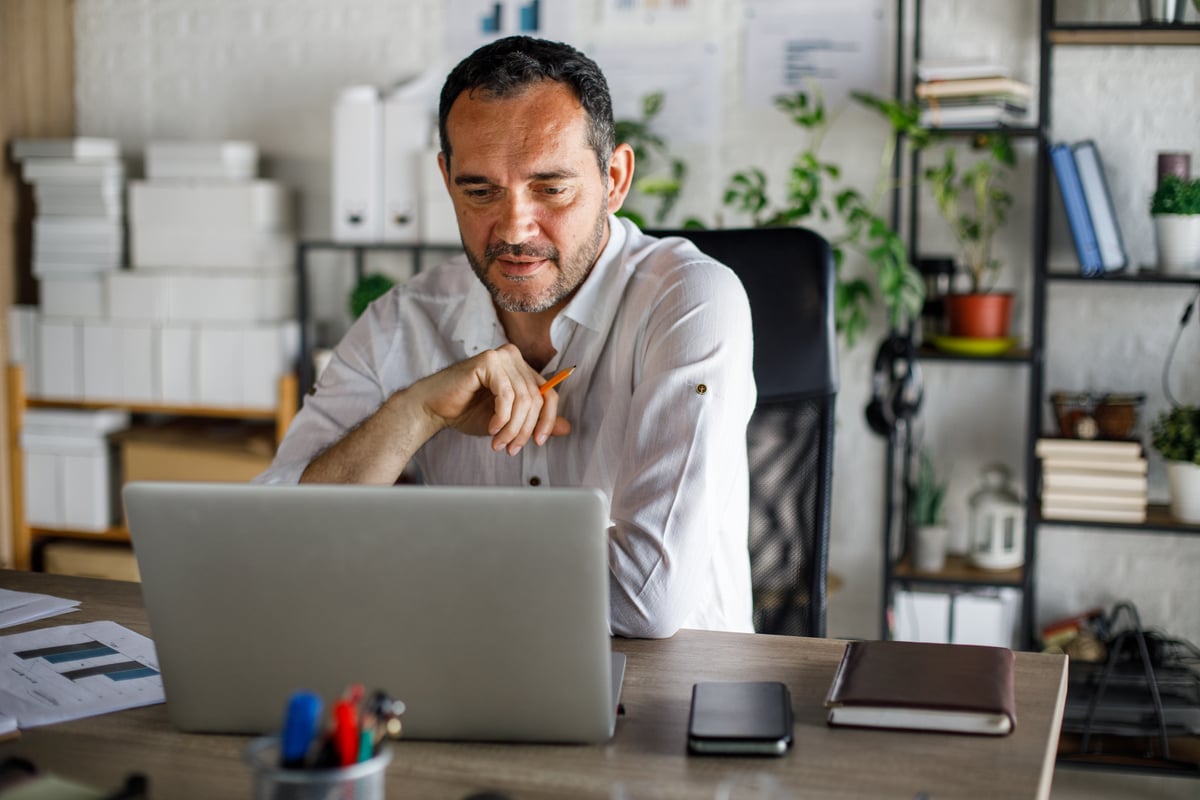 Person sitting at a desk  and looking at a laptop. 