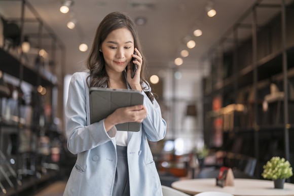 A person checks a tablet while talking on a phone.