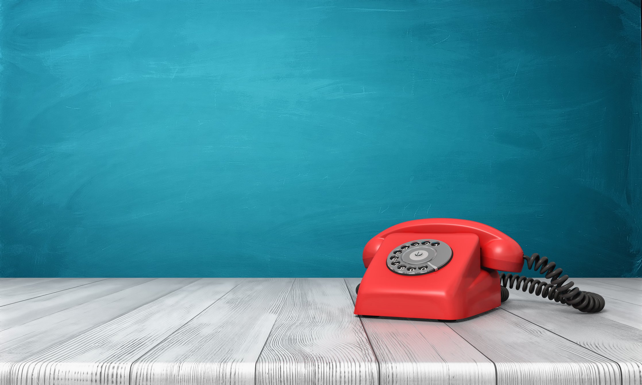 Red rotary dial telephone on a grey table.