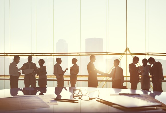 Professionals meet in a boardroom with the sun setting in the background.