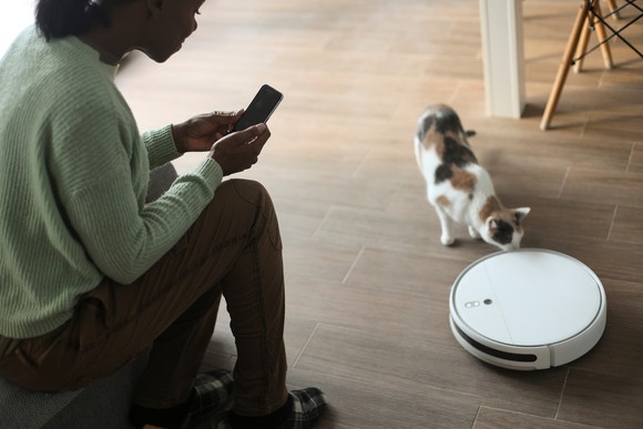 Person taking picture of a cat investigating a Roomba.