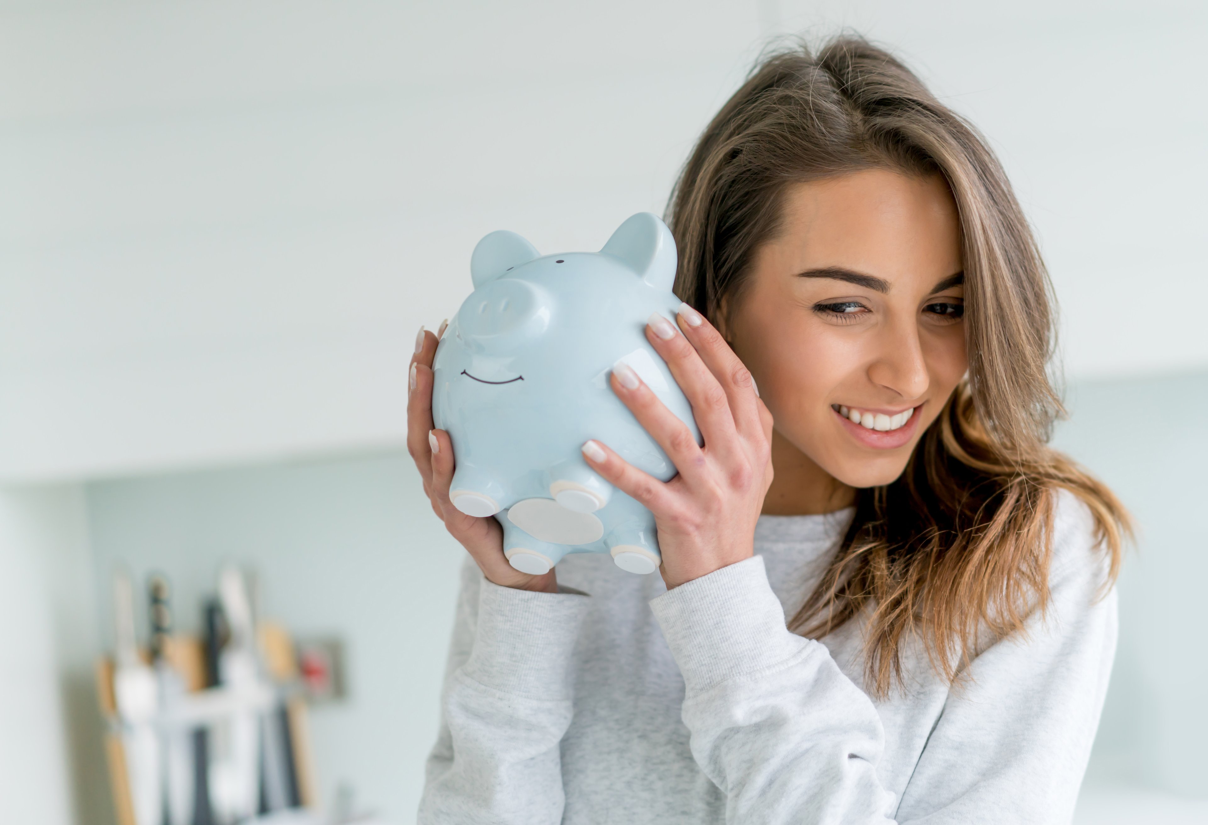 A smiling person holds a piggy bank.