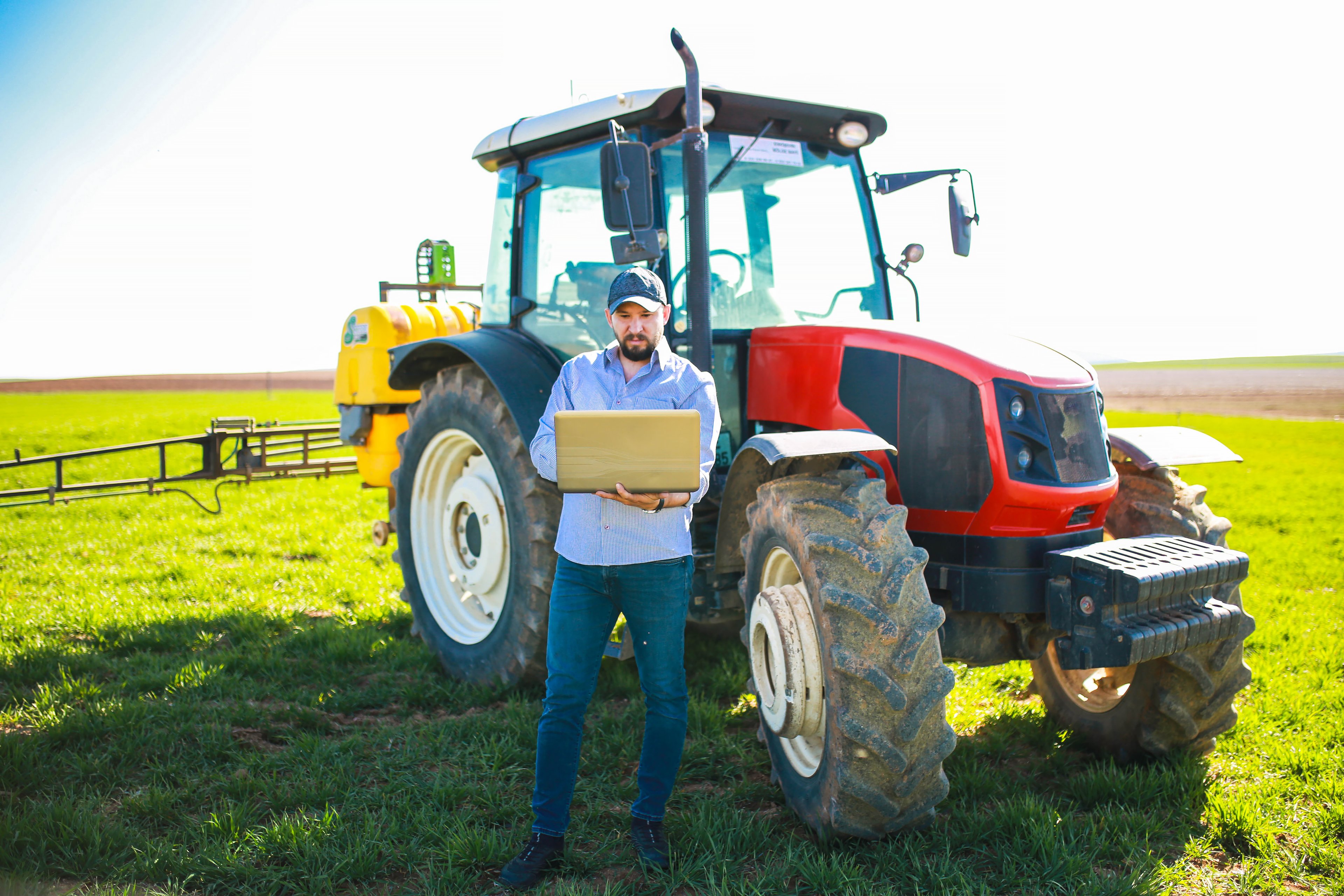 Person holding laptop next to tractor in field.