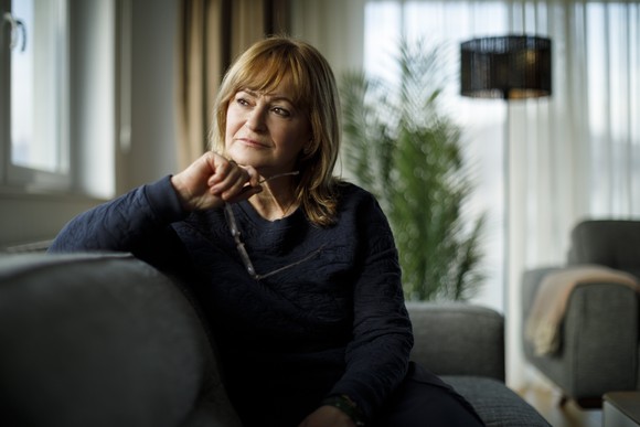 Person with a serious expression sitting on couch, looking off into the distance.