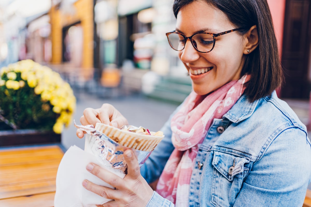 Woman prepares to eat while seated on a bench near flowers.