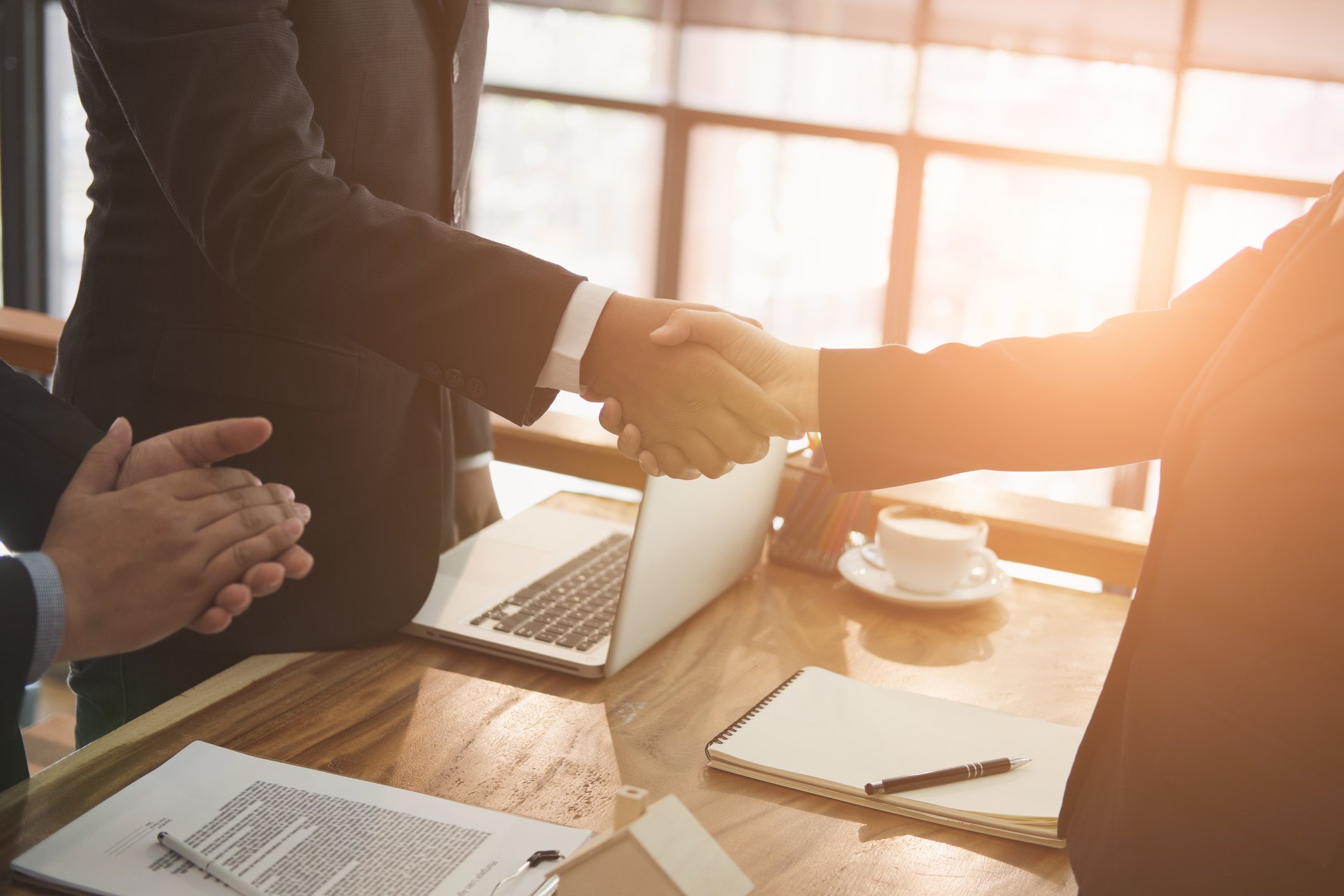 Two people in suits shaking hands over a table