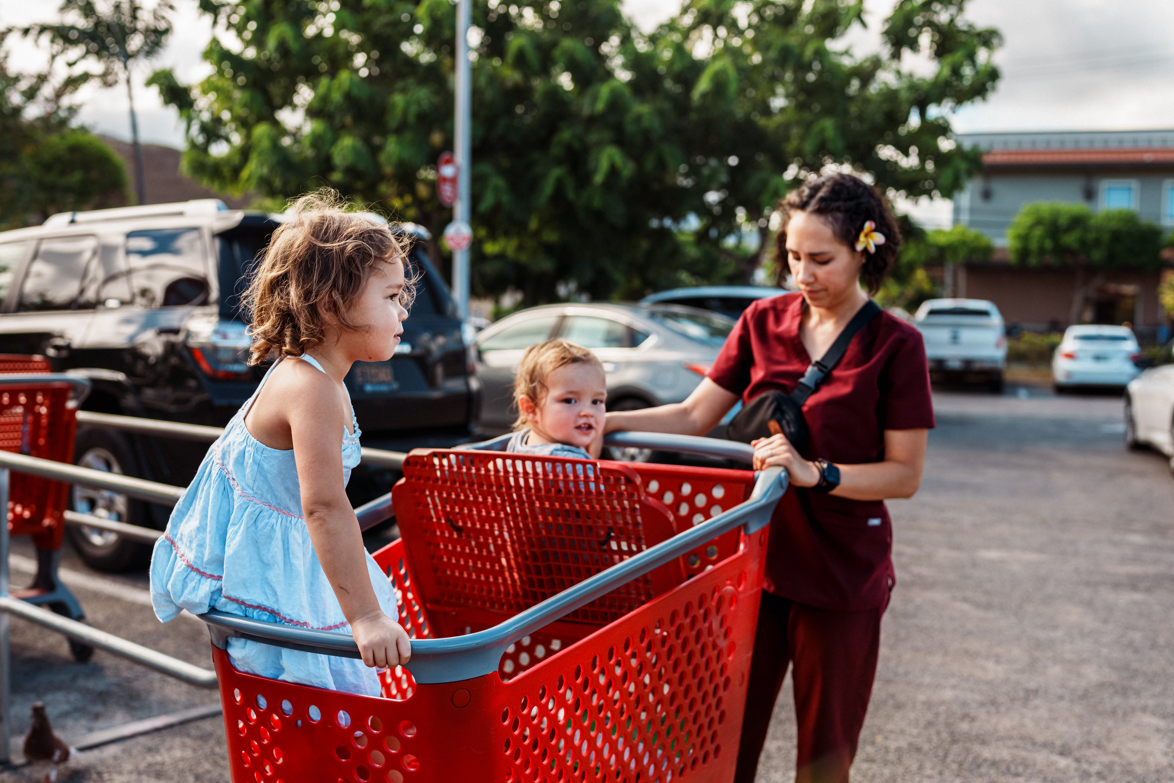 A person pushes a shopping cart with two children riding in it. 