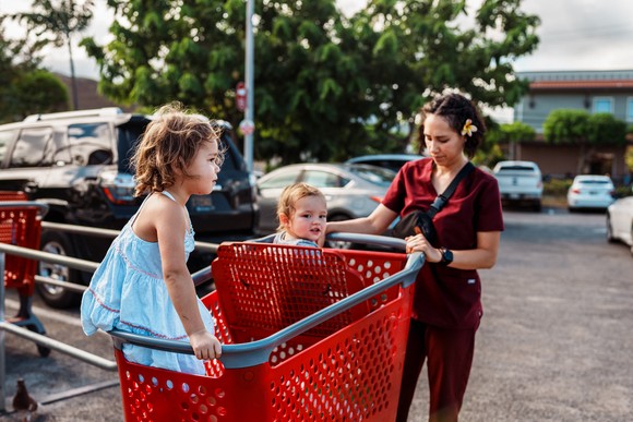 A person pushes a shopping cart with two children riding in it. 