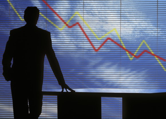 A man stands before a large chart with two lines in downward trends. 