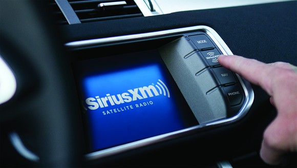 A person pressing the satellite-radio button on their in-car dashboard. 