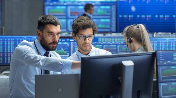 Stock traders pointing at a monitor in a trading room. 