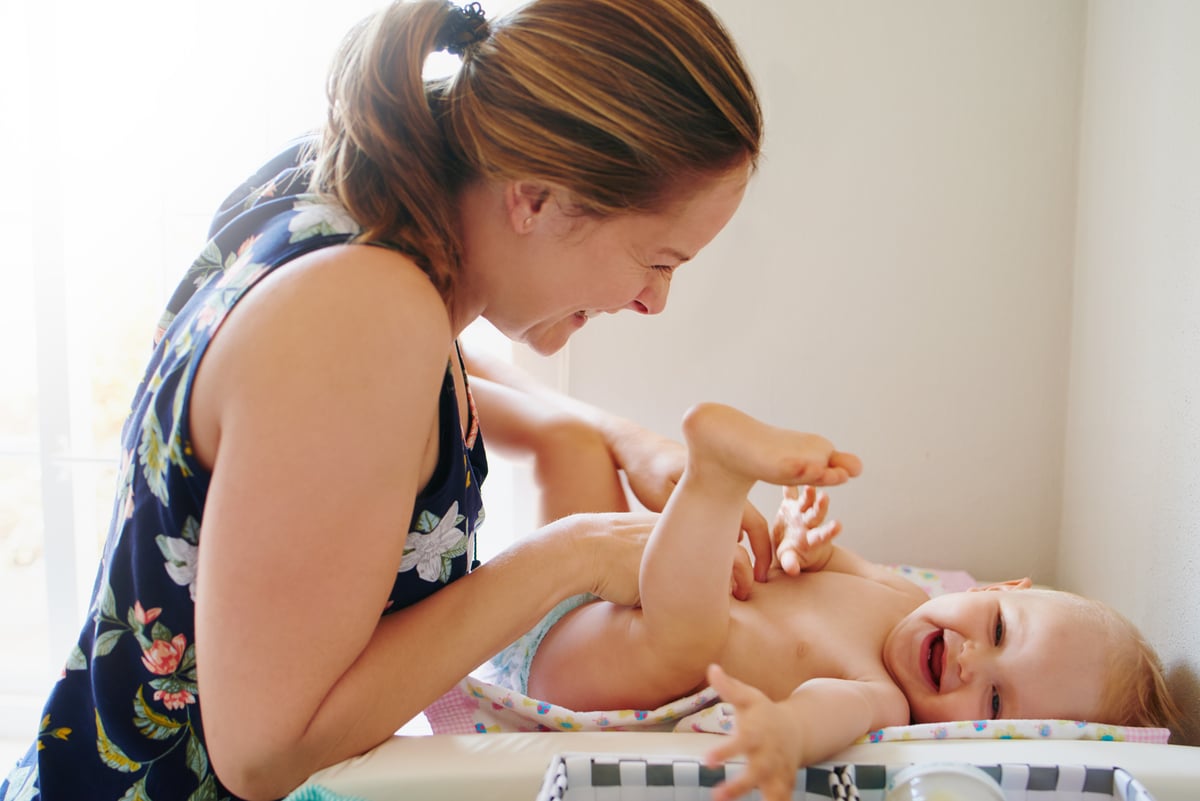 A baby smiles while an adult changes its diaper. 