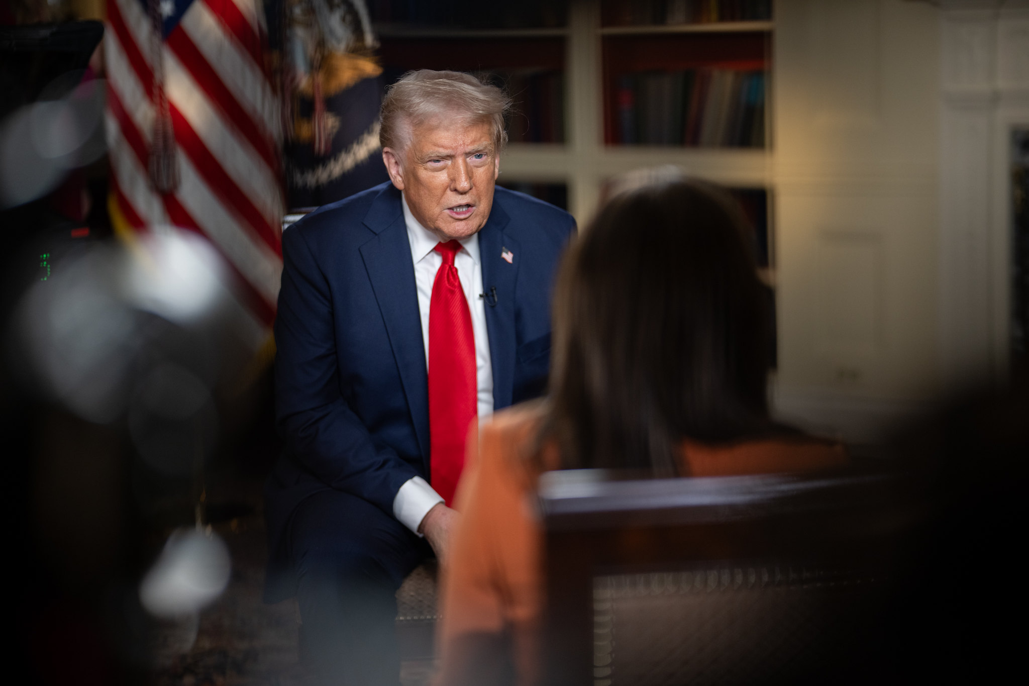President Donald Trump sitting in front of an American flag and facing an interviewer.