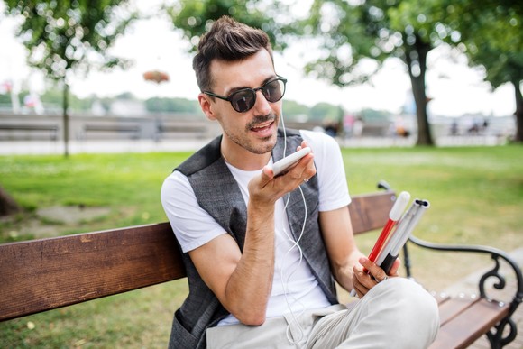 A person sits on a bench while speaking into a smartphone.