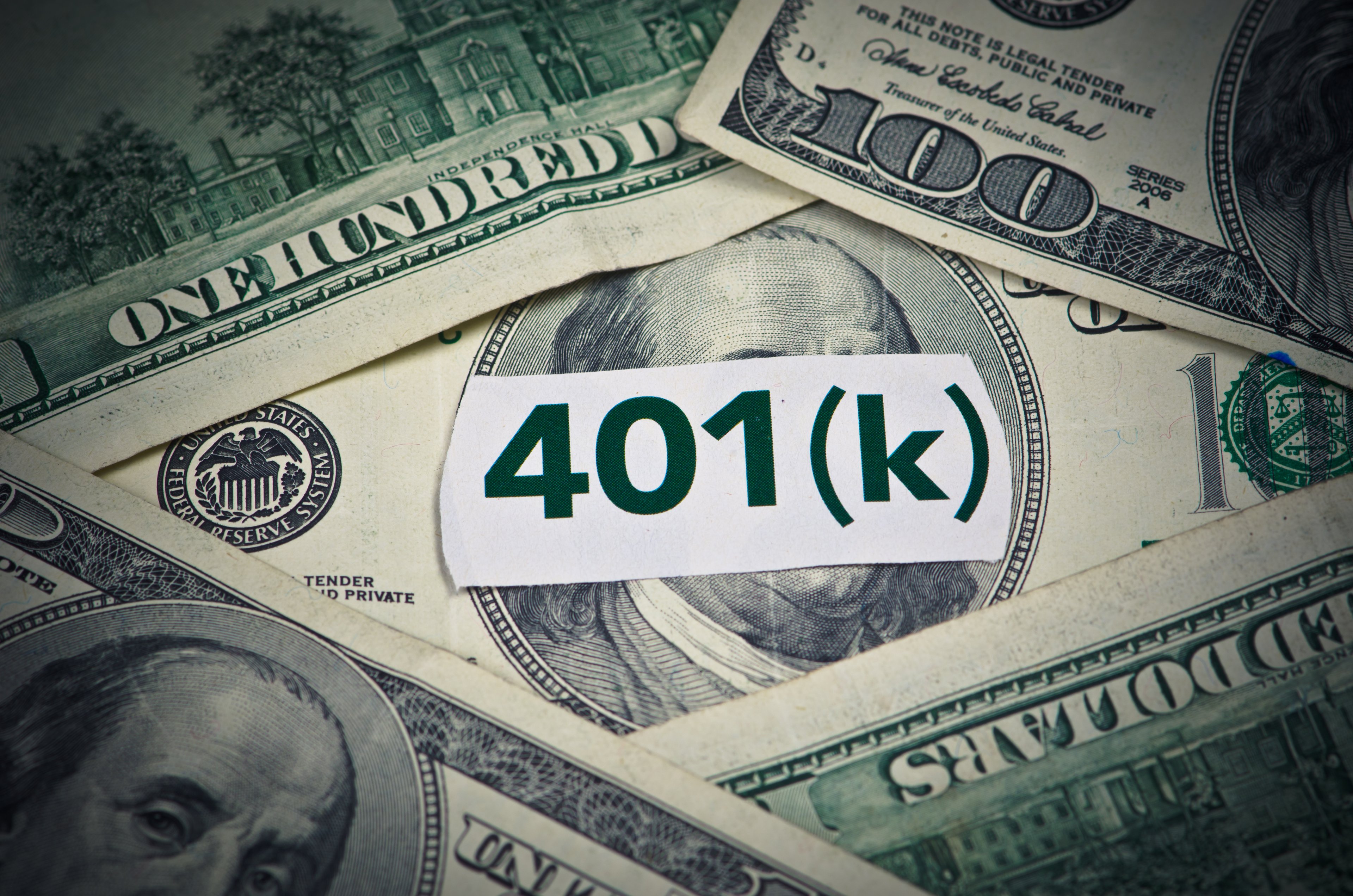 A white label reading "401(k)" laying on top of $100 bills. 