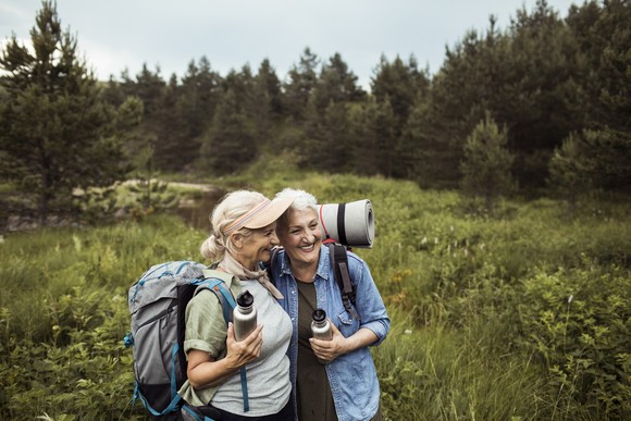Two older adults standing in a field with backpacks.