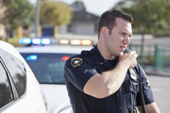 A police officer speaks into a land-mobile radio (LMR) while on duty.