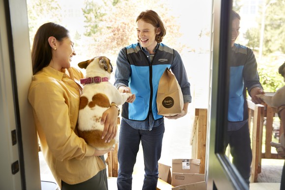 An Amazon delivery person bringing a package to a customer holding a dog.