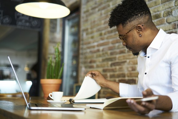 An investor studies a pair of notebooks while sitting in an office in front of a laptop.