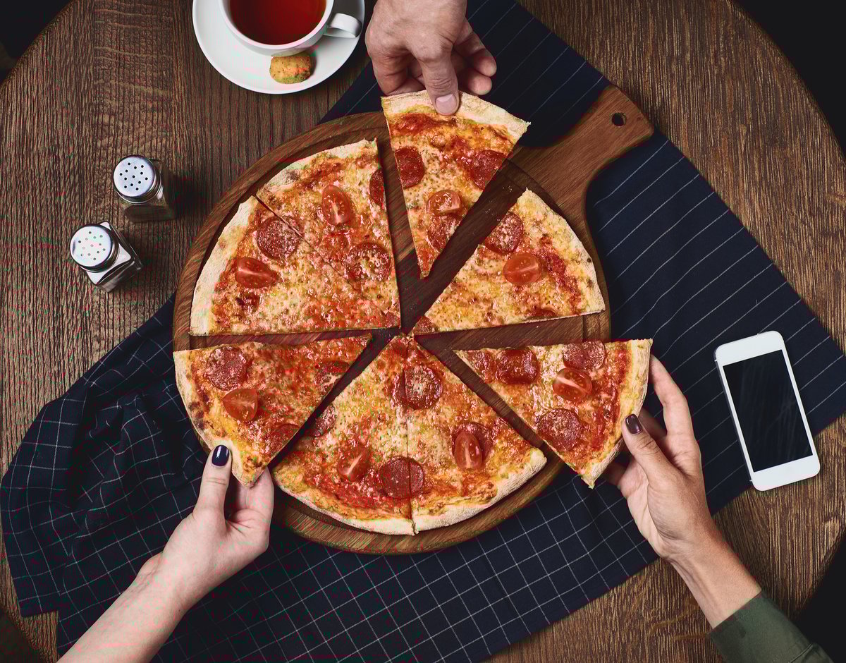A group of people grabbing a slice of pizza from a table.