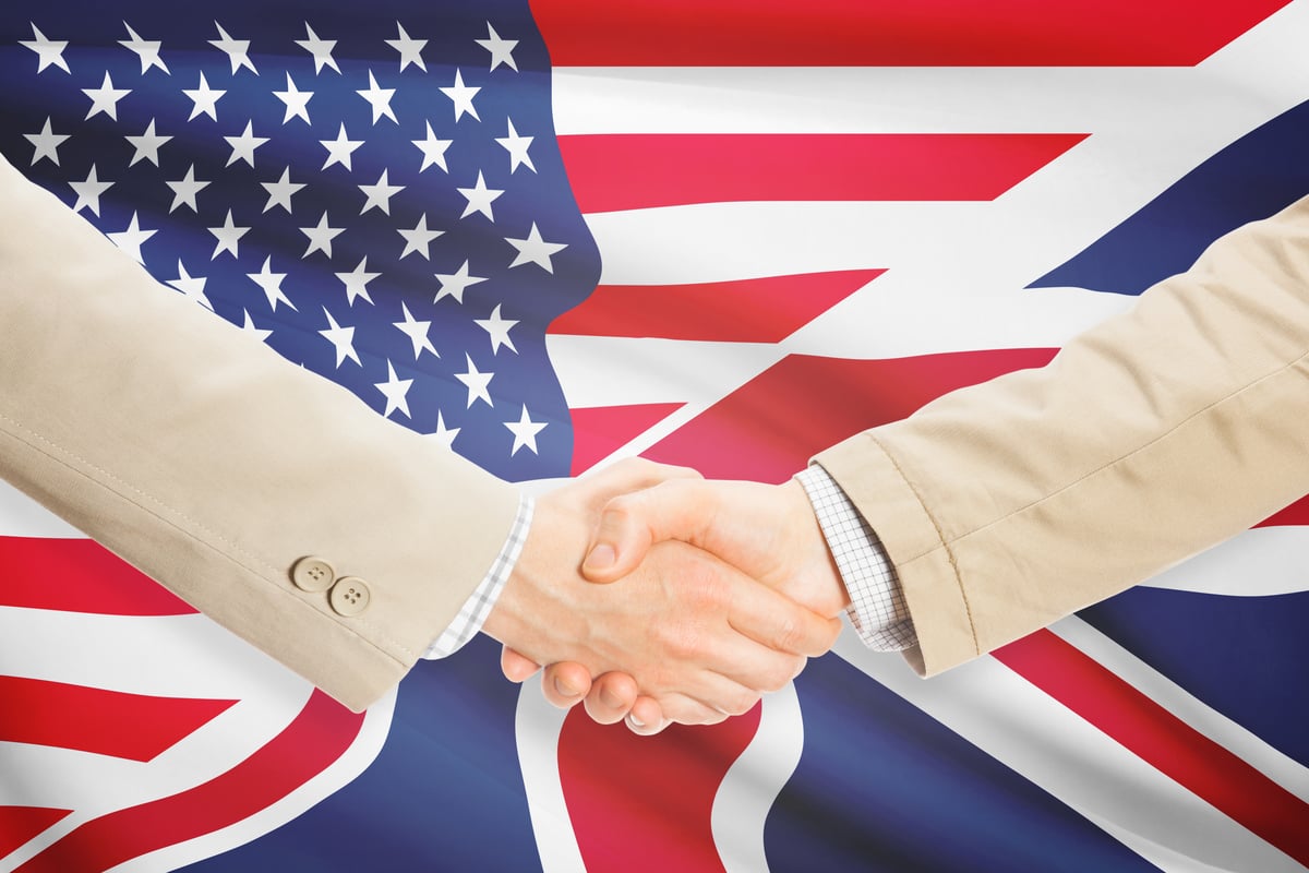 Two hands shake in front of American and British flags.