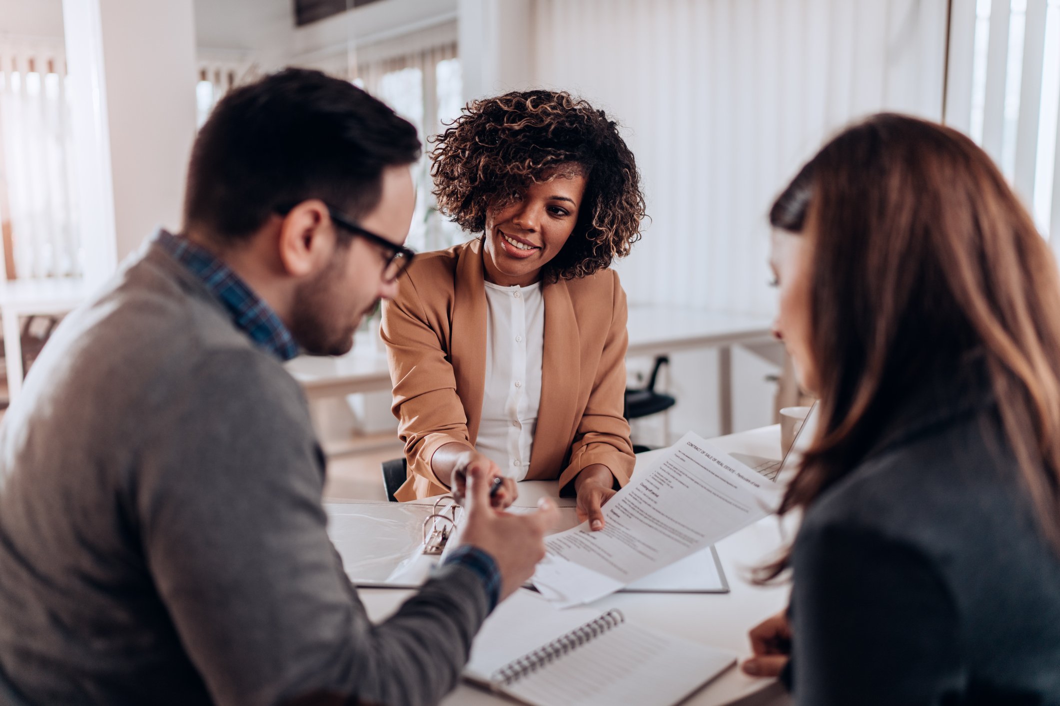 Three coworkers sit around a table looking at papers in an office.