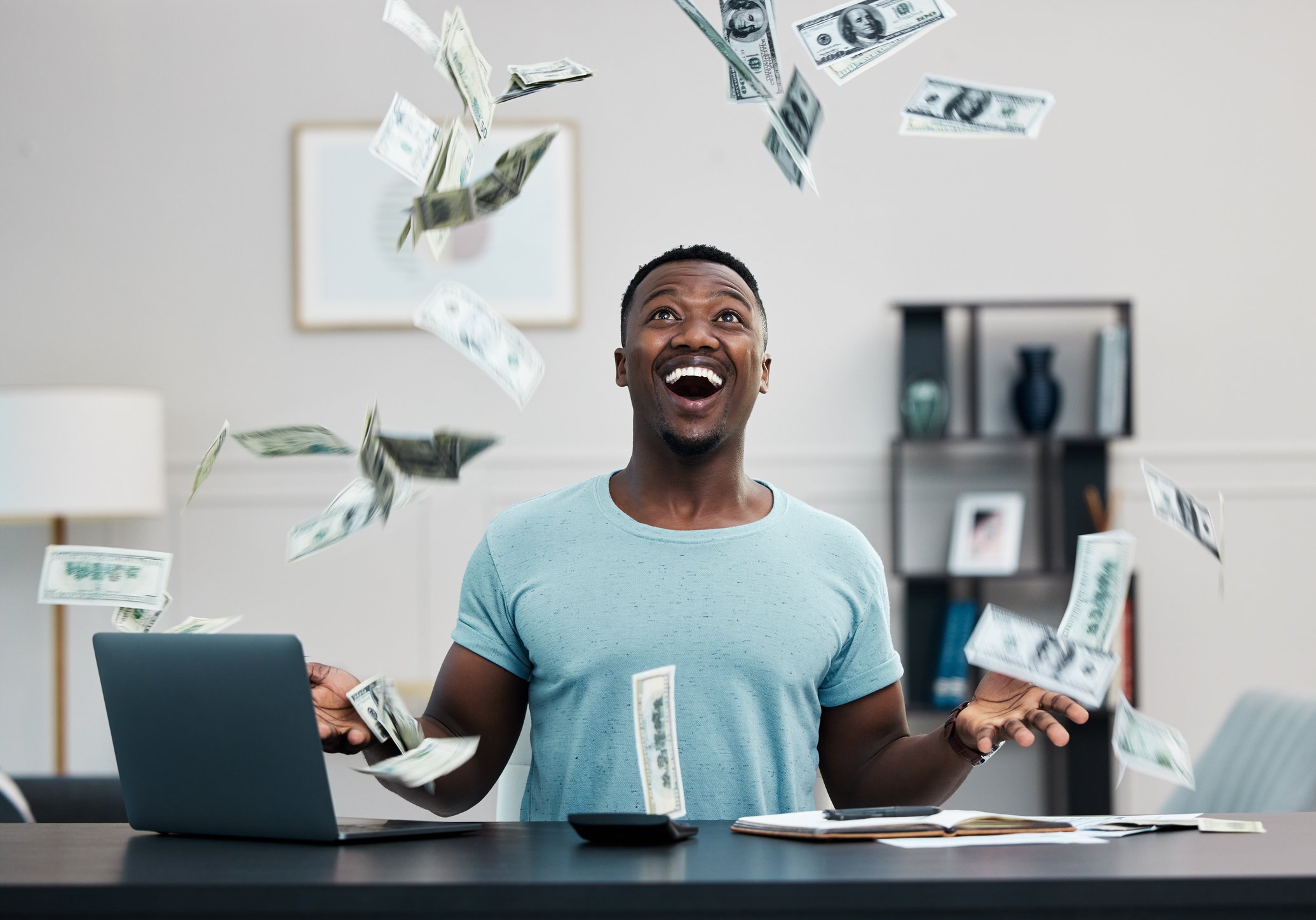 Investor sitting at a desk catching dollars falling out of the sky.