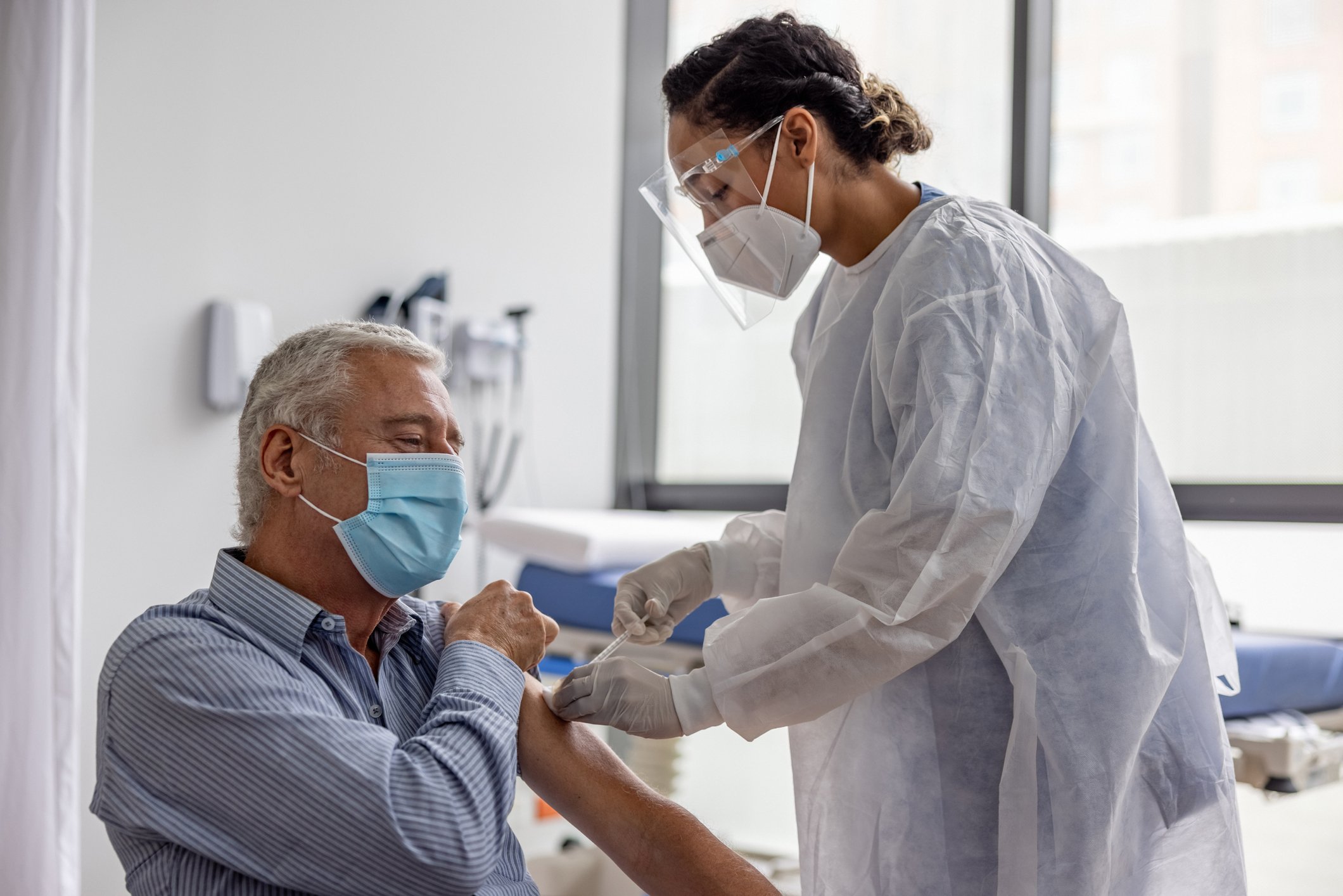 Healthcare worker in personal protective equipment vaccinating a patient.