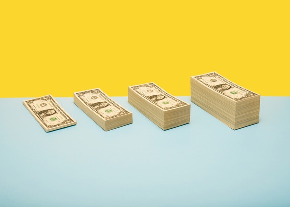 Four stacks of dollar bills growing larger in size.