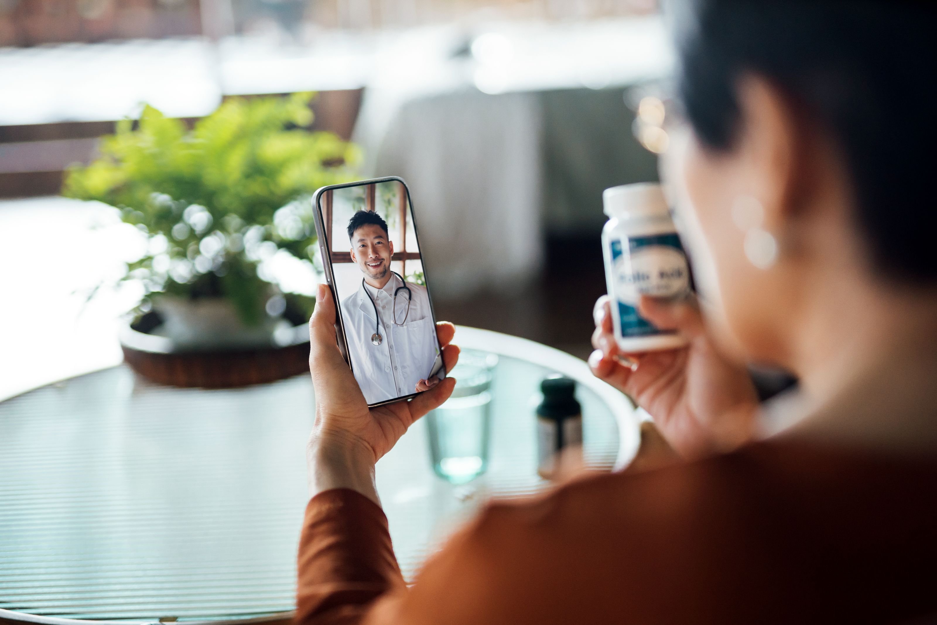 A person holds up a bottle of medicine while on a telehealth call with their doctor on a smart phone.