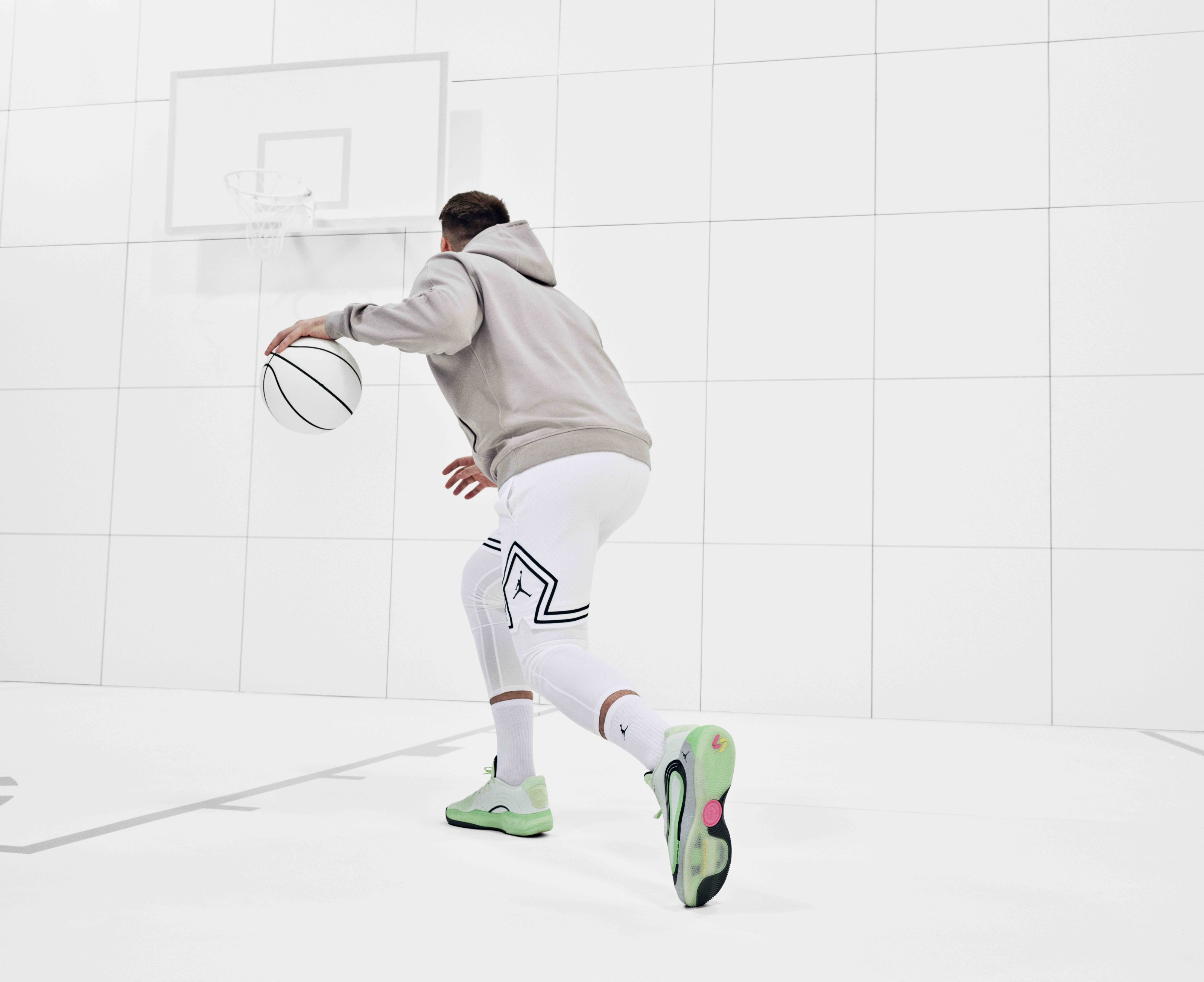 Luka Dončić wearing Nike sneakers and workout clothes while dribbling a white basketball in a white room.