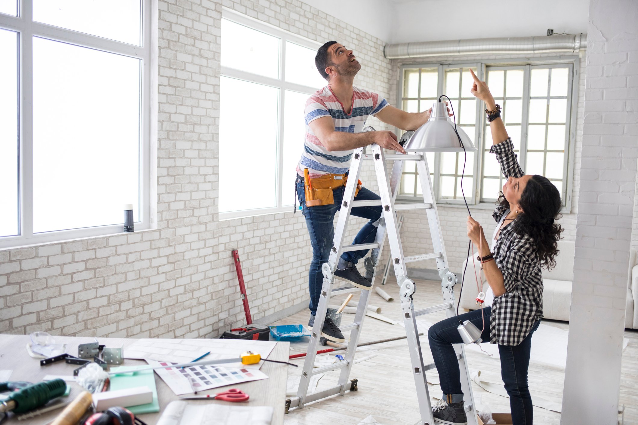 Two people working with ladder and tools on a home renovation project.