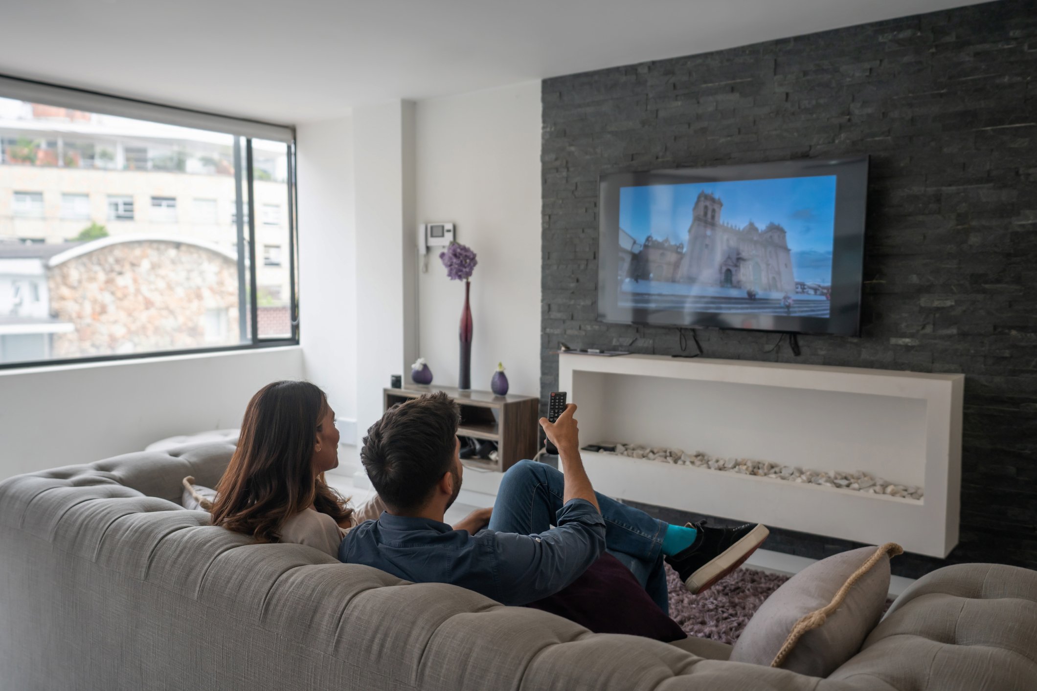 A couple sits on a couch in the living room, watching TV.