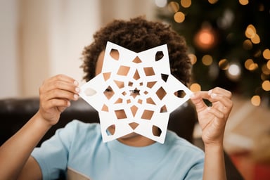 Little kid peering through a paper snowflake