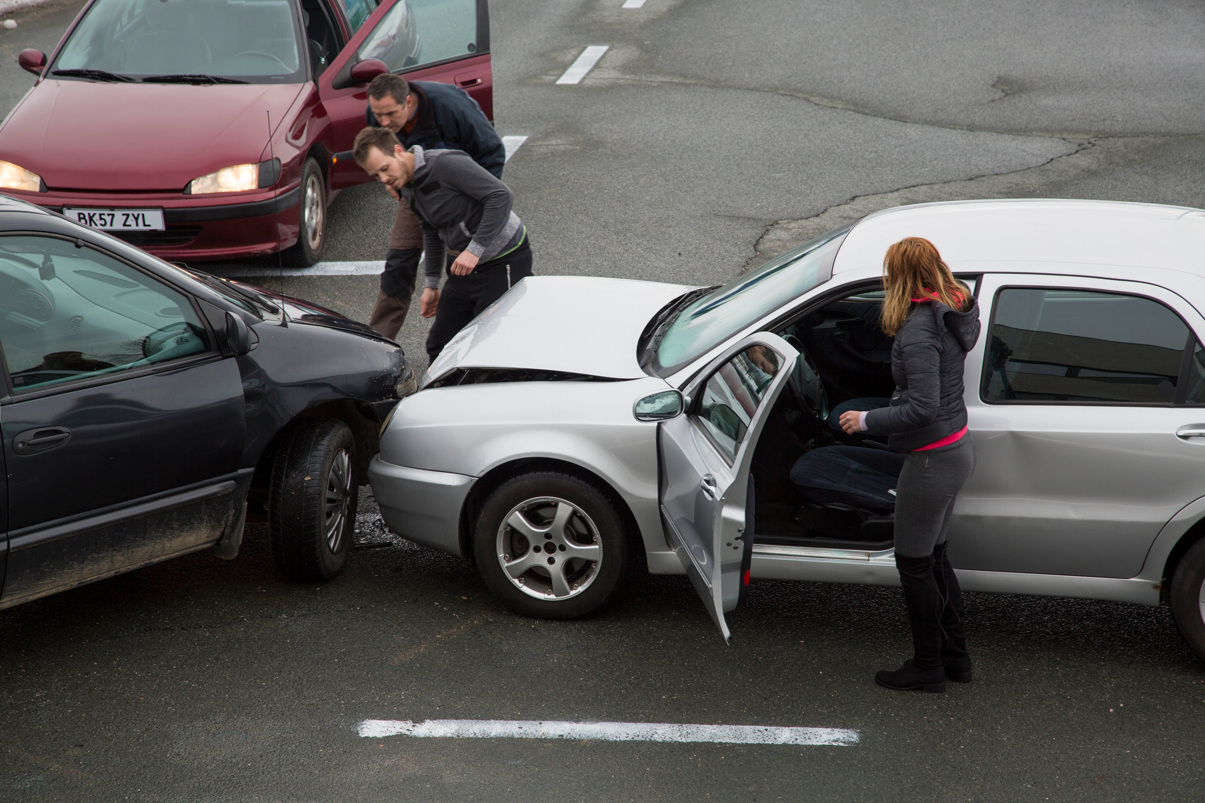 Three drivers talk to each other after being involved in a collision at an intersection.