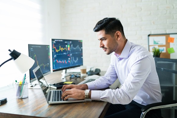 An investor sits at a desk while typing on a computer.