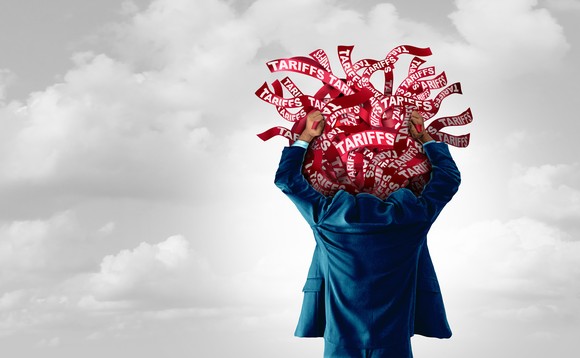 A person wearing a suit holds a tangle of red ribbons that say Tariffs above their head.