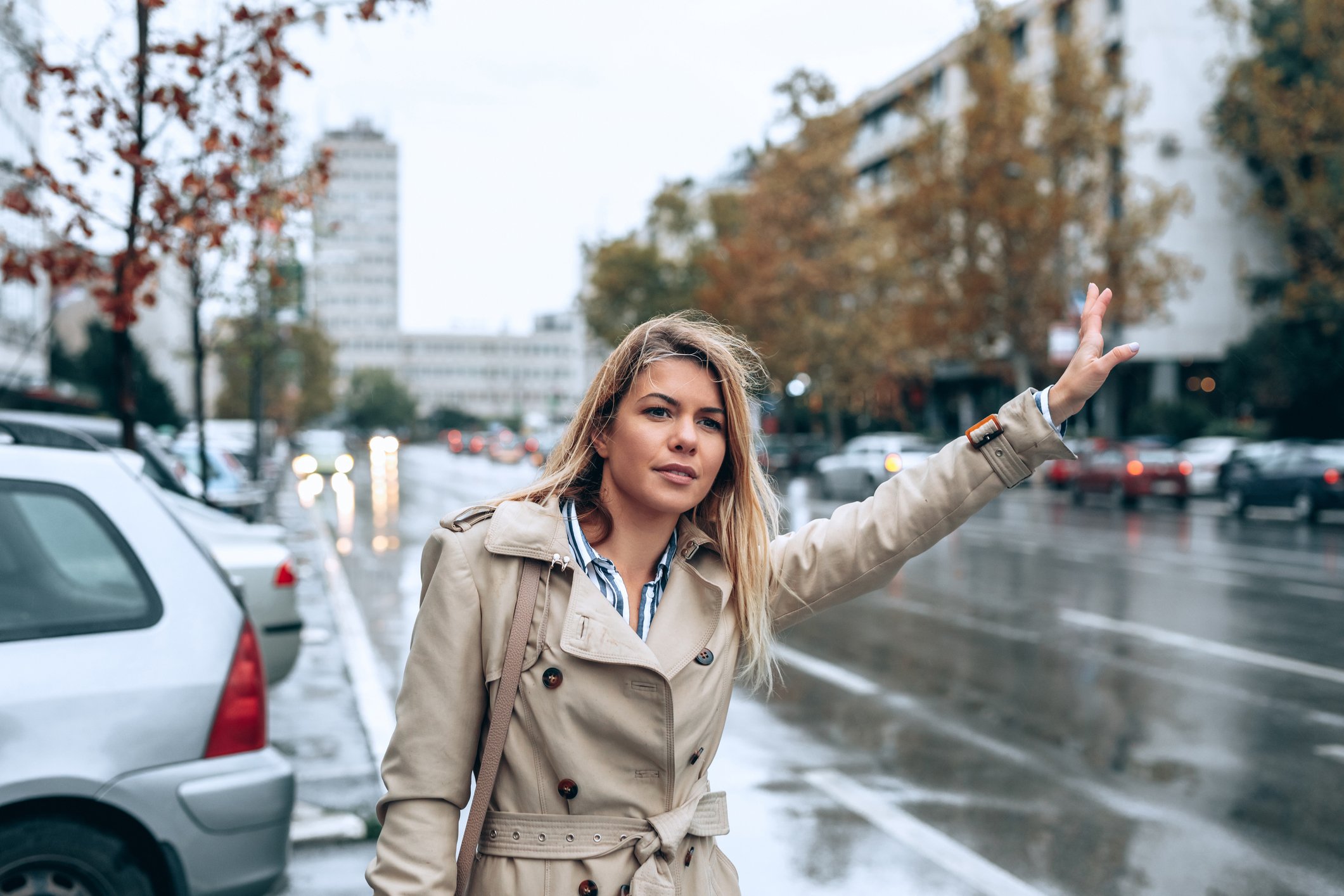 A person waving down a car ride on the street on a rainy day.