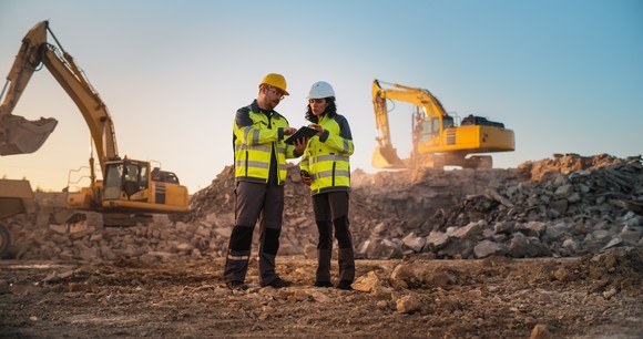Construction workers in a field with equipment in the background.