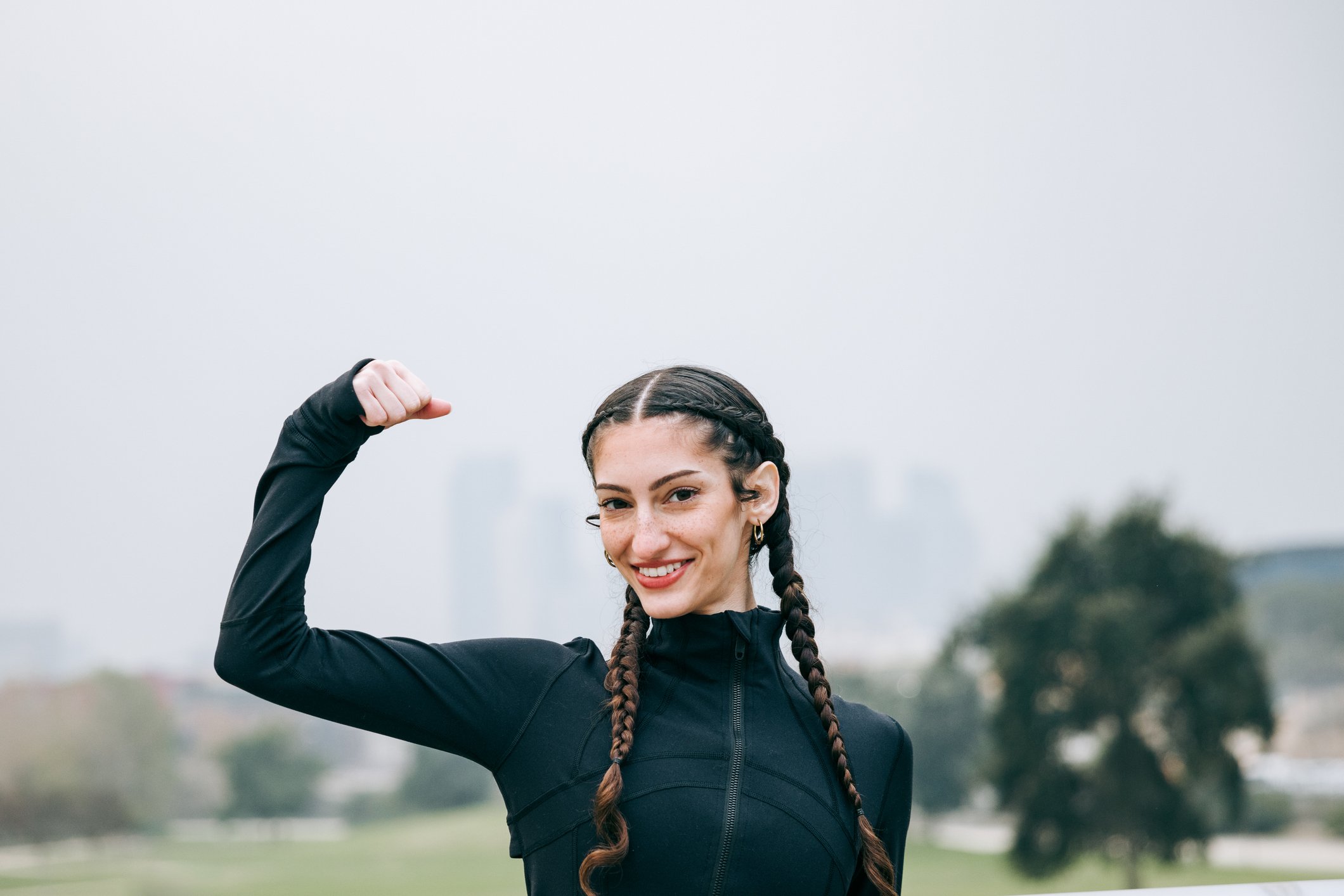 A person flexing their bicep while standing outside.