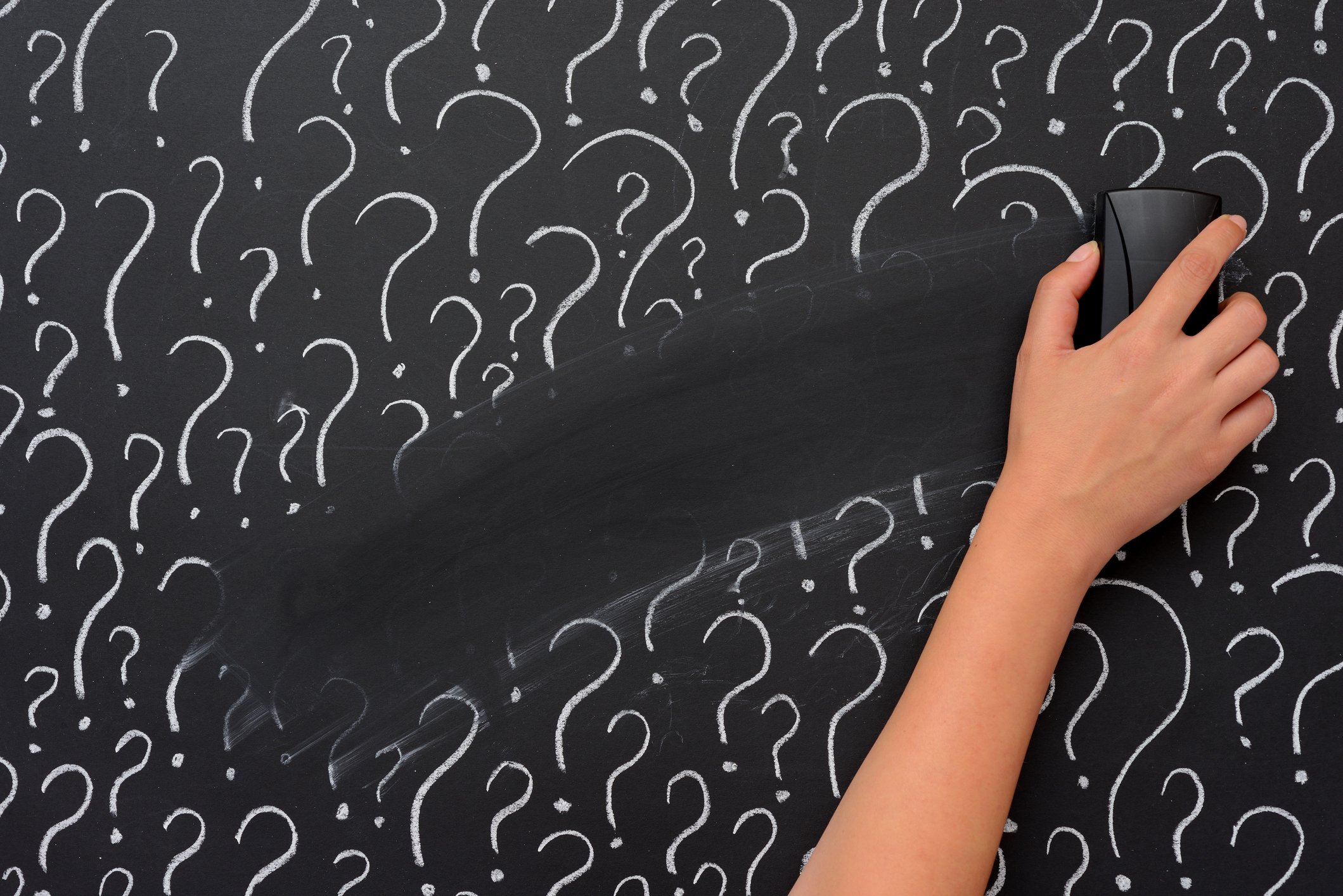 A hand erasing chalk question marks from a blackboard.