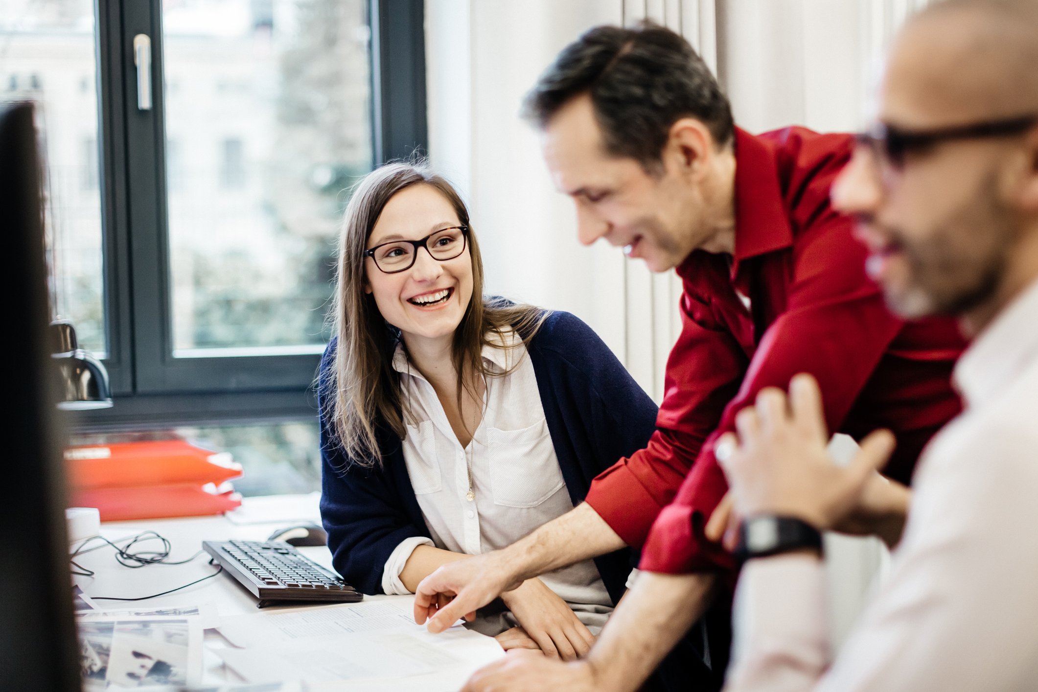 Three colleagues are engaged in a cheerful discussion, while one is looking at laptop.