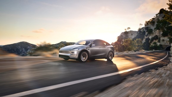 silver new Model Y driving on scenic coastal road. 