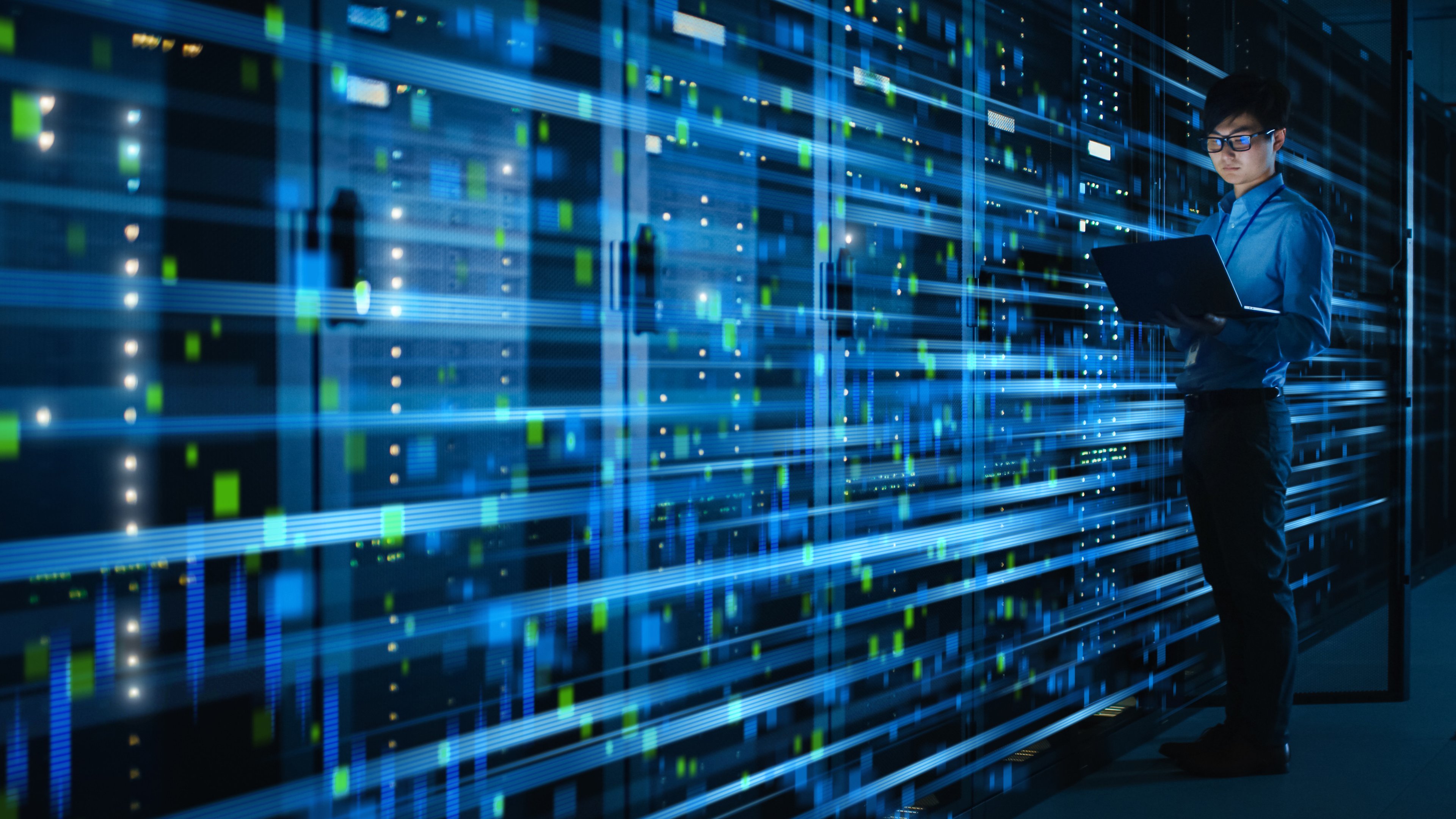 Worker with laptop in AI cloud data center with blue streaking lights. 