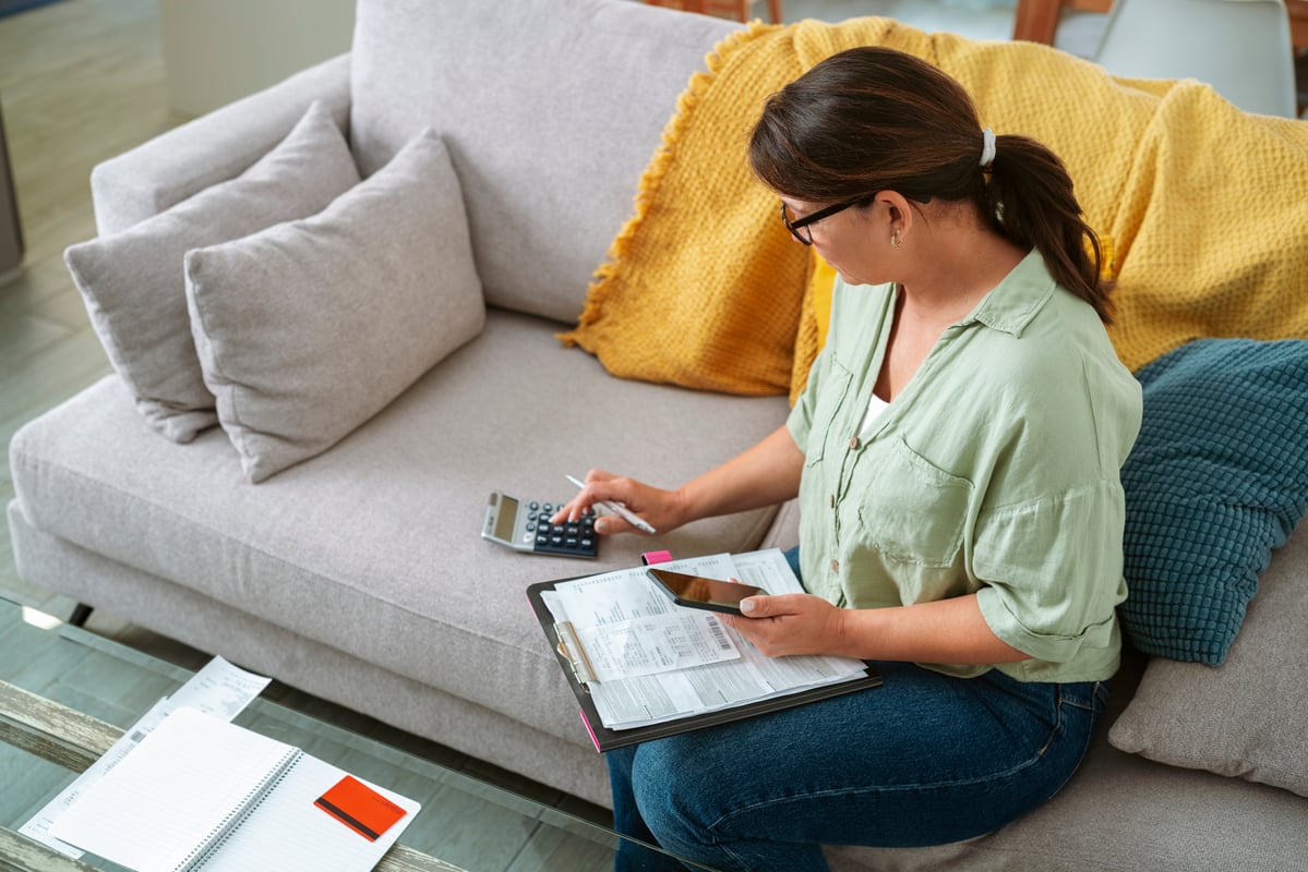 A person punching buttons on a calculator while holding a phone.