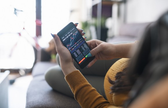 lying down on couch, looking at stock chart on phone.