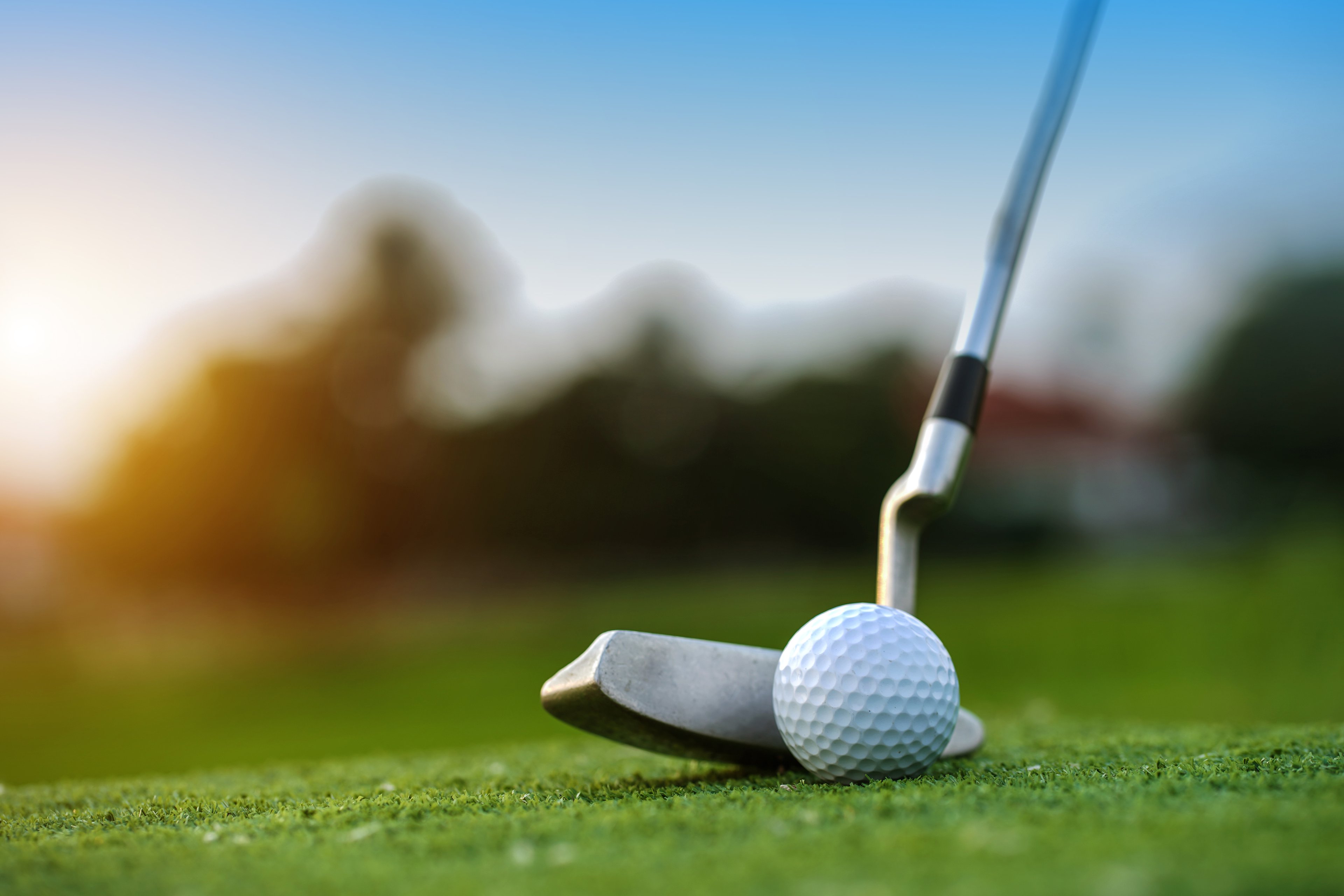Close up of a putter right behind a golf ball