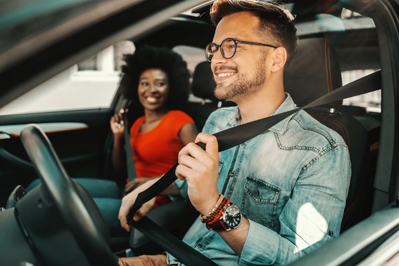 Two people put on their seat belt while sitting in a car.