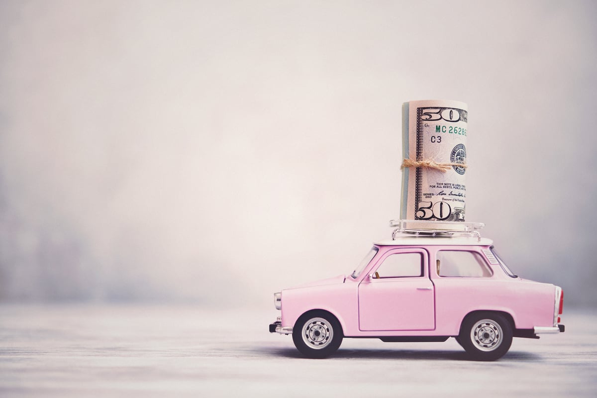 A small pink car with a giant roll of money on it.